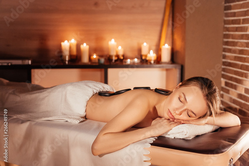 Beautiful young woman enjoying relaxing treatments the stone therapy at the spa salon by candlelight. The concept of relaxing and rejuvenating procedures