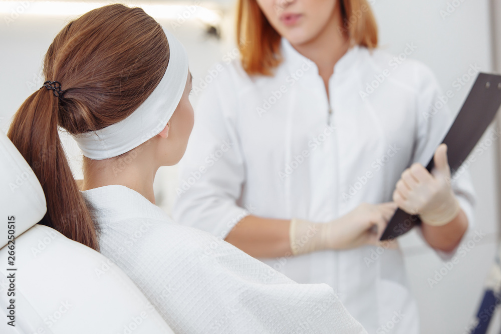 Fototapeta premium Young pretty woman came to a beauty salon and consults with a beautician on anti-aging treatments. Self care concept