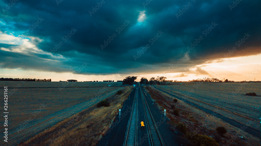 Person in Yellow Jacket on Old Train Tracks With Epic Sky