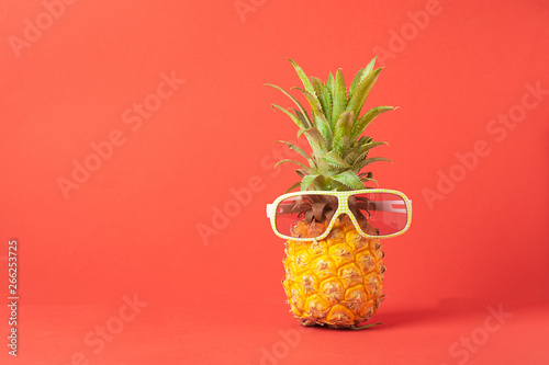Yellow ripe pineapple in dark sunglasses on a red background. Funny face from a tropical fruit. Concept Copy space.