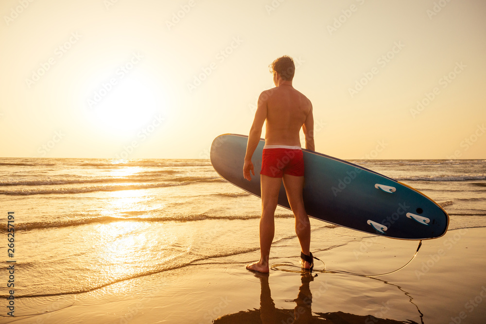 surfer with surfboard looking at sunset at Goa India