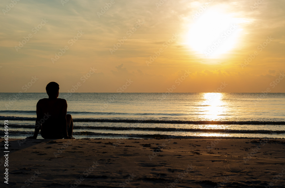 The silhouette photo of a man sitting alone on the beach enjoy sunrise moment with the reflection on the sea in summer season. The silhouette photo of a man sitting alone on the beach enjoy sunrise moment with the reflection on the sea in summer season.