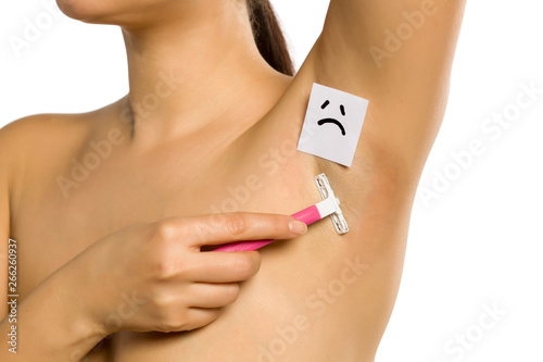 Woman shave  her underarm with a sad face on her on white background © vladimirfloyd