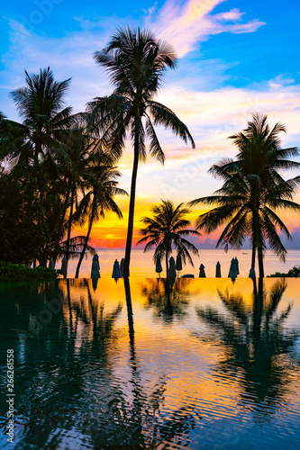 Beautiful outdoor nature landscape with sea ocean and coconut palm tree around swimming pool at sunrsie or sunset