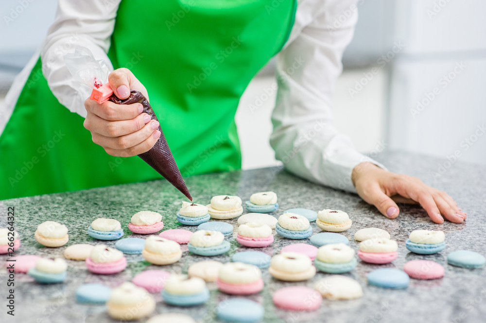 Closeup chef with confectionery bag squeezing cream filling to macarons shells Closeup chef with confectionery bag squeezing cream filling to macarons shells