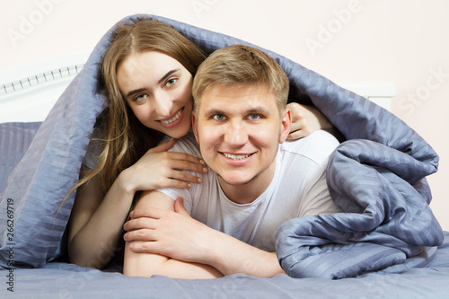 Happy couple is lying in bed under the blanket together