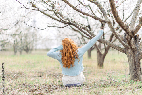 Wallpaper Mural Romantic young woman in white dress and blue sweater is sitting on the ground in spring blooming garden. Back view. Torontodigital.ca