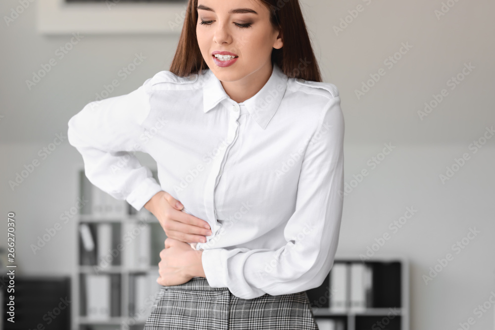 Young woman suffering from abdominal pain in office Young woman suffering from abdominal pain in office