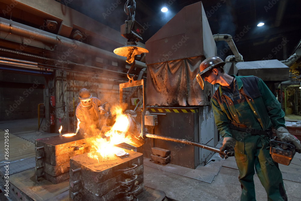 Arbeiter in einer Giesserei am Schmelzofen beim gießen eines metallischen Werkstückes // Worker in a foundry at a melting furnace casting a metallic workpiece 