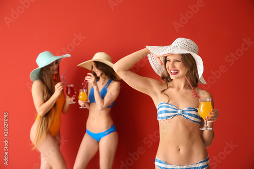 Beautiful young women in swimsuits and with cocktails on color background