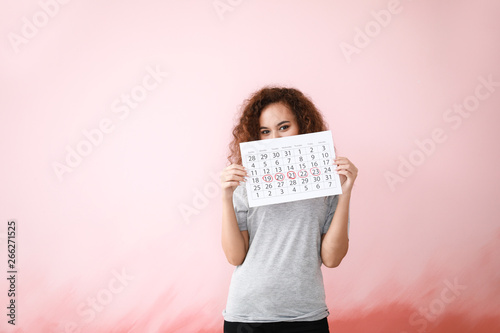 African-American woman holding calendar with marked days of menstruation on color background