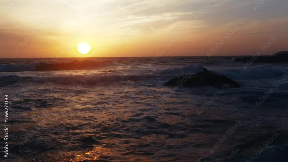Gliding close to beach and water as waves crash against rocks and shore at sunset Gliding close to beach and water as waves crash against rocks and shore at sunset