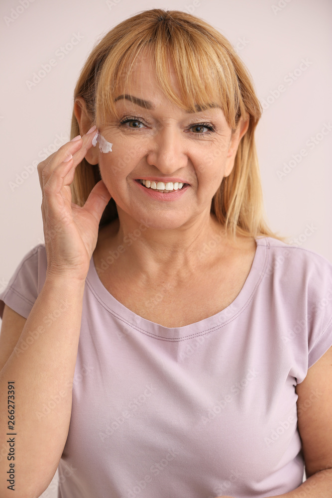 Mature woman applying facial cream against color background