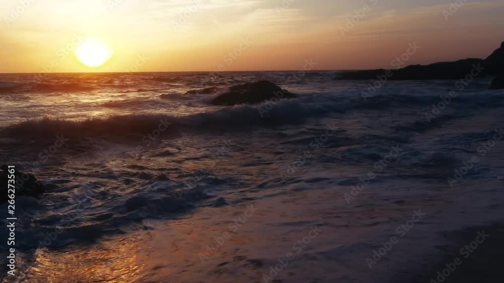 Gliding close to beach and water as waves crash against rocks and shore at sunset Gliding close to beach and water as waves crash against rocks and shore at sunset