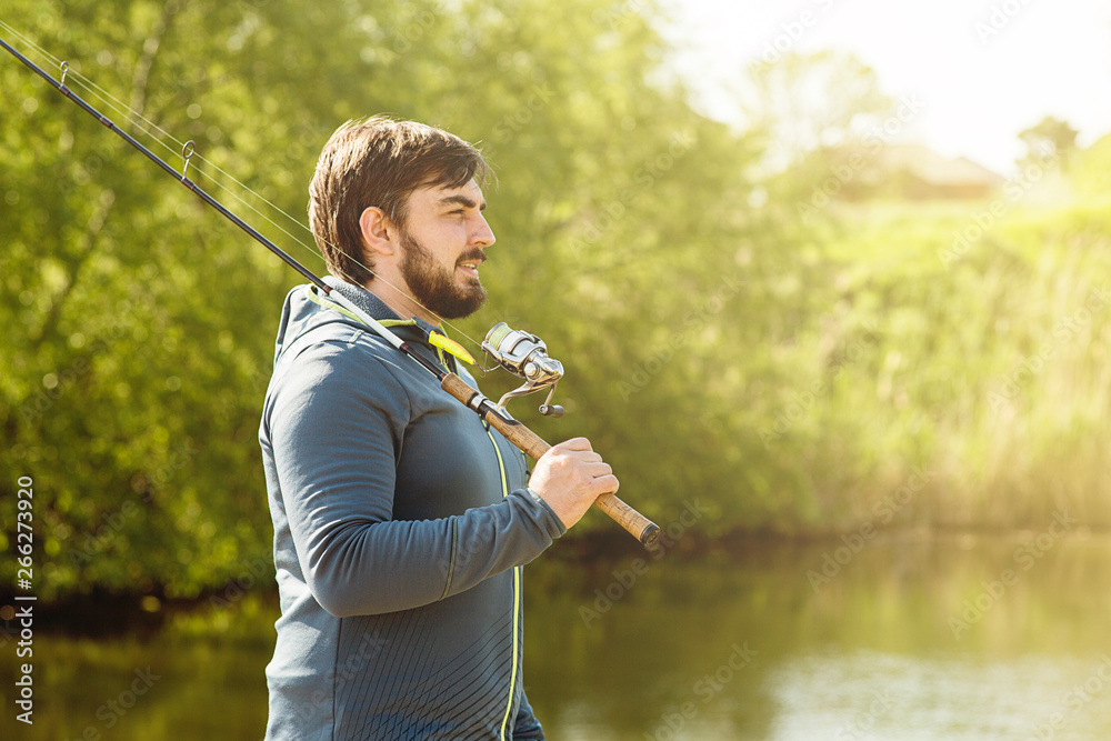 a man on a Sunny day goes fishing, holding a fishing rod on his shoulder - obrazy, fototapety, plakaty 