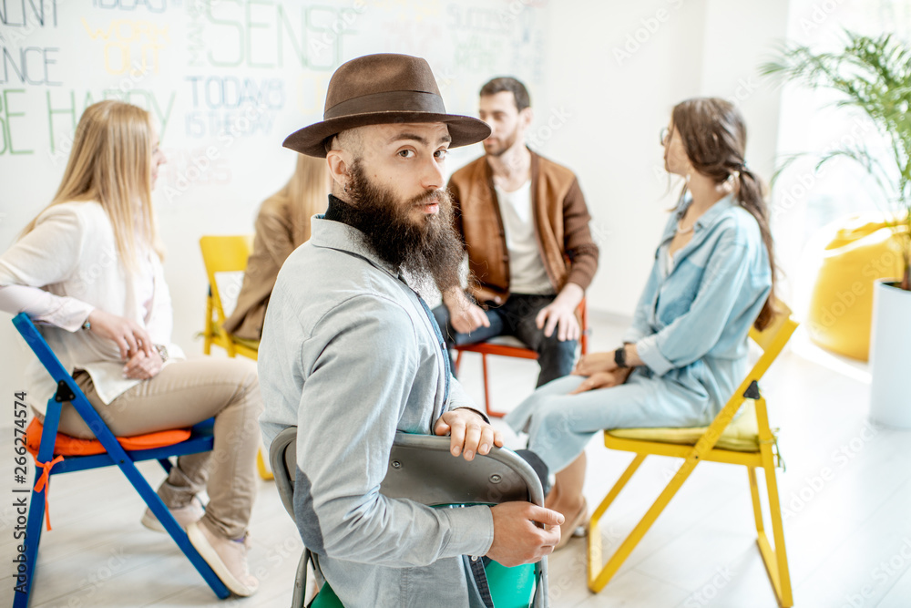 Portrait of a handsome man sitting in a circle with group of people during the psychological training in the white office