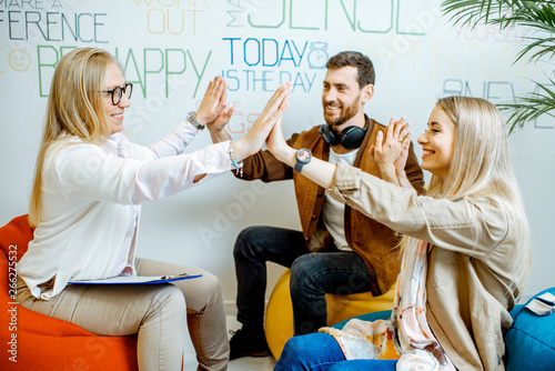 Young and happy couple giving five with hands during the psychological counseling with senior female psychologist in the modern office