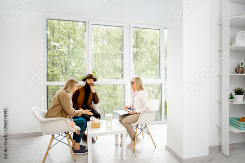 Young couple with psychologist sitting during the mental therapy in the white spacious office. Wide interior view