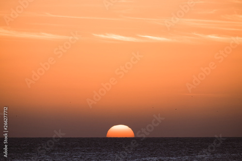 Classic tropical sunset or sunrise on the sea horizon with sun and water touching together - orange warm sky in background - travel destination paradise holiday concept