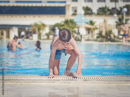 Happy cheerful European boy on side of swimming pool.