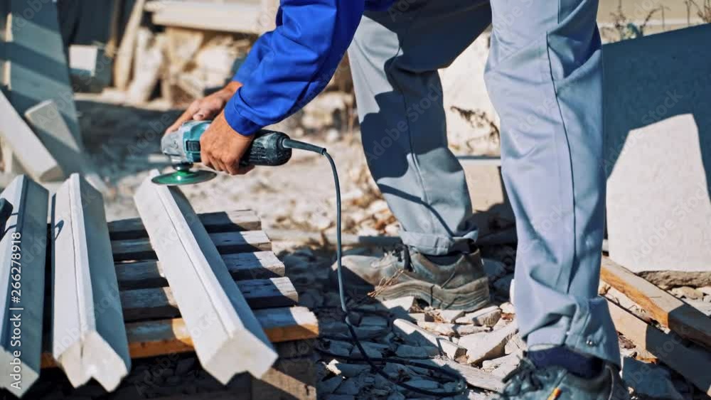 Laborer polishes stone with hand grinder outdoors. Man worker is polishing stones by hand grinding machine on the open air. Laborer polishes stone with hand grinder outdoors. Man worker is polishing stones by hand grinding machine on the open air.