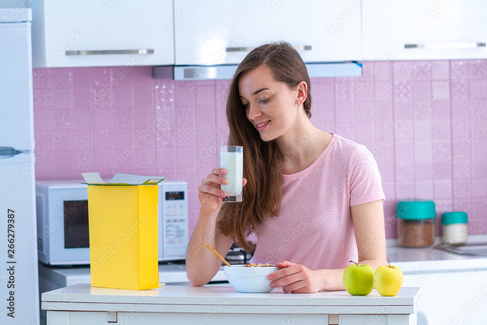 Happy attractive woman holding glass of fresh milk and spoon of crispy chocolate balls for cereals breakfast in early morning in kitchen at home Happy attractive woman holding glass of fresh milk and spoon of crispy chocolate balls for cereals breakfast in early morning in kitchen at home