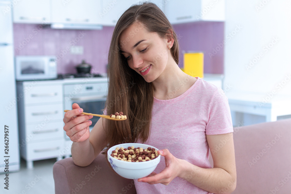 Portrait of young, happy beautiful brunette woman in pajamas eating chocolate balls for cereals breakfast at home Portrait of young, happy beautiful brunette woman in pajamas eating chocolate balls for cereals breakfast at home