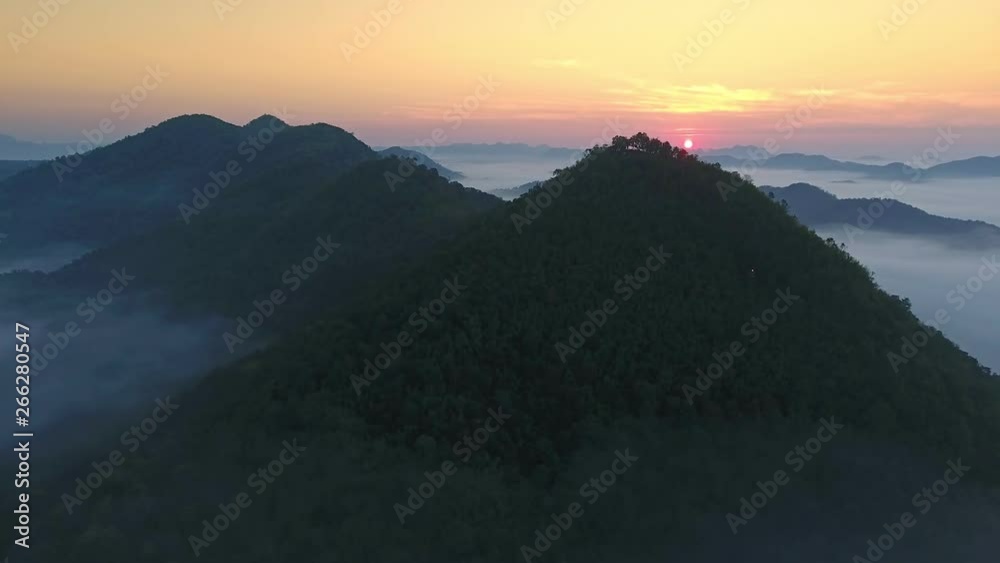 Aerial view shot by drone fly above a mountain range, slowly reveal the sun rises in the morning surrounded by sea of haze or fog, dense forest peak / ridge top spectacular scenery with sea of mist Aerial view shot by drone fly above a mountain range, slowly reveal the sun rises in the morning surrounded by sea of haze or fog, dense forest peak / ridge top spectacular scenery with sea of mist