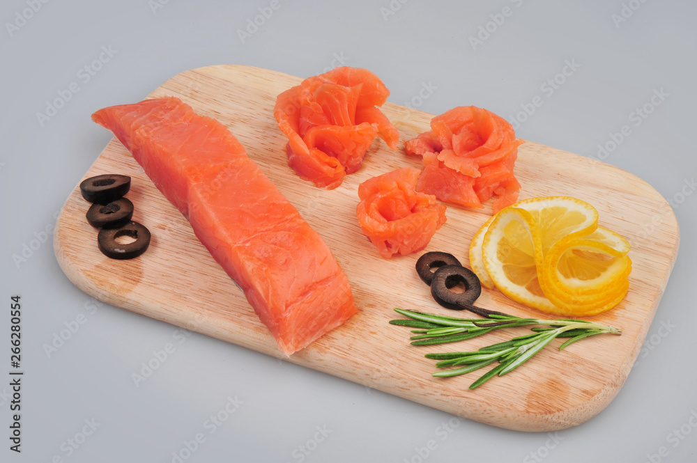 Fresh salmon decorative roses fillets, with lemon, olives on the board. Isolated on a gray background