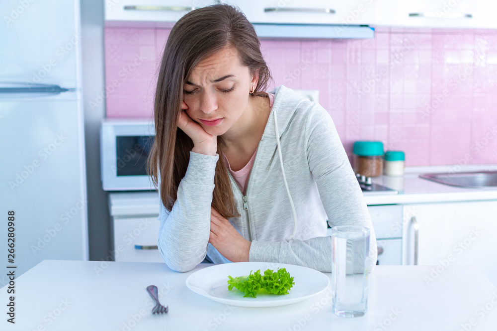 Sad unhappy young woman is tired of dieting and not wanting to eat organic, clean healthy food