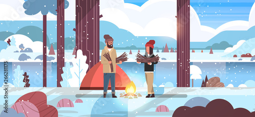 couple tourists hikers holding firewood man woman organizing fire near camp tent hiking camping concept winter landscape nature river mountains background flat horizontal full length