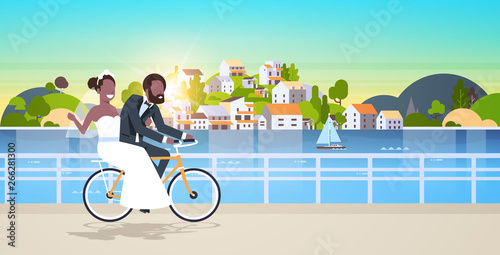 just married man woman riding bicycle romantic african american couple bride groom cycling bike having fun wedding day concept mountain city island background full length horizontal flat