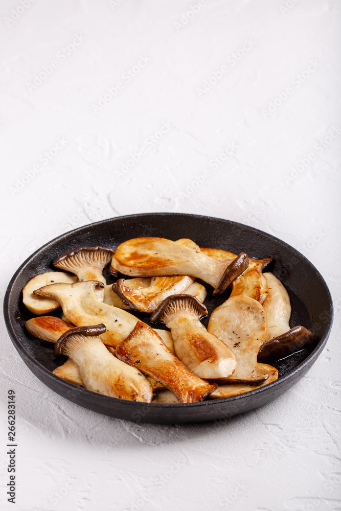 Fried eryngii mushrooms in cast-iron pan on white table. Grilled slices of king oyster mushrooms. Copy space. Fried eryngii mushrooms in cast-iron pan on white table. Grilled slices of king oyster mushrooms. Copy space.