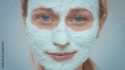 macro portrait of young woman with face covered eith facial blue mask. atching to the camera. Facial cleansing treatment mask. photo