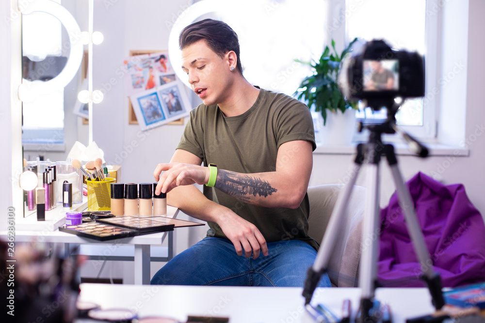 Communicative interested man having different makeup products on the table Communicative interested man having different makeup products on the table