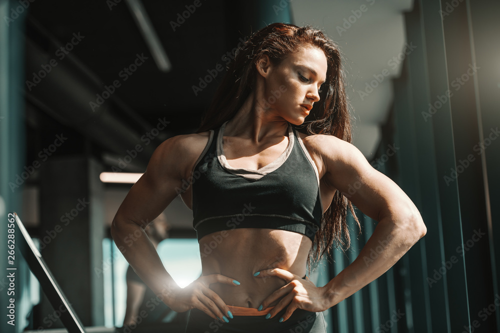 Portrait of beautiful Caucasian female bodybuilder posing with hands on  hips in gym. You are the creator of your own destiny. Stock Photo