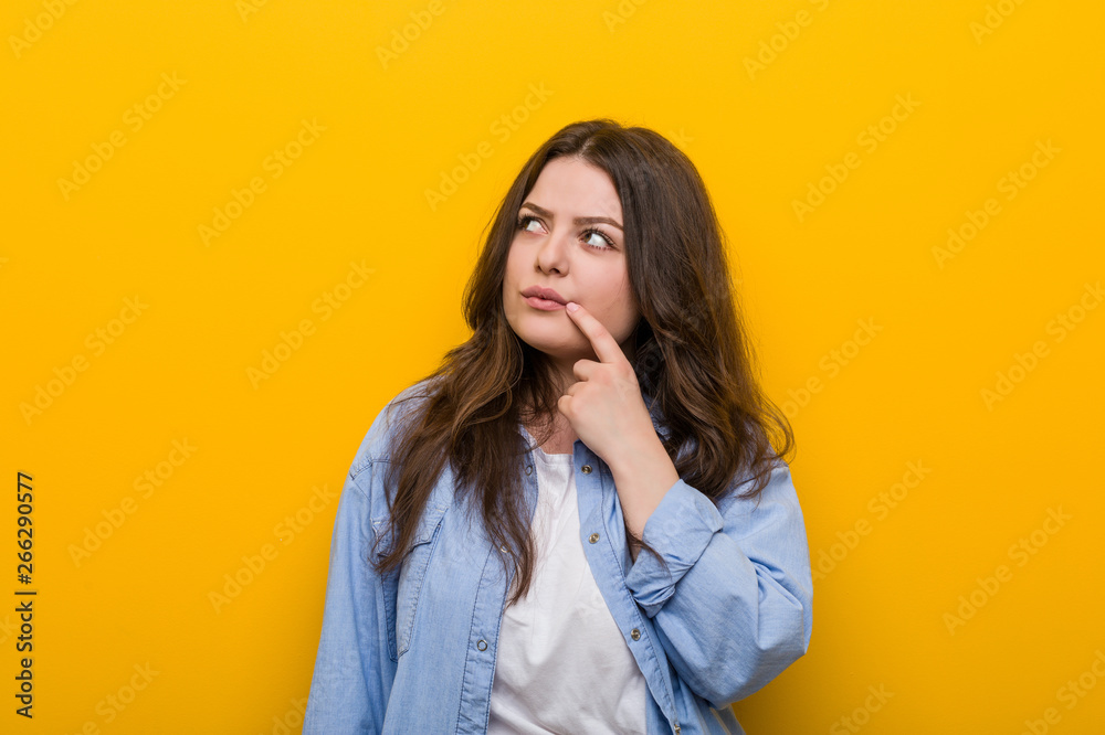 Young curvy plus size woman looking sideways with doubtful and skeptical expression.