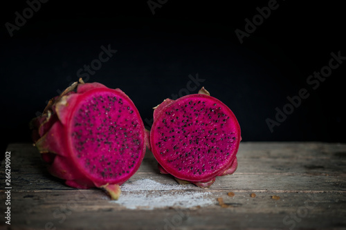 Red Dragon fruit on wooden surface, solid black background, still life shooting style.