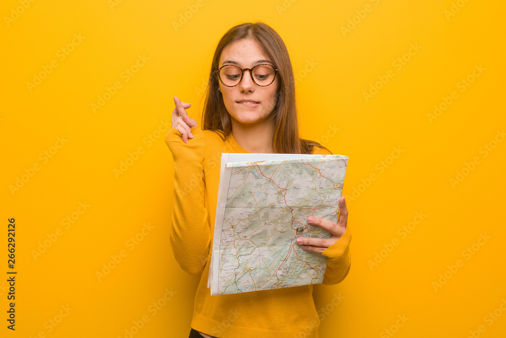 Fototapeta premium Young pretty caucasian woman crossing fingers for having luck. She is holding a map.