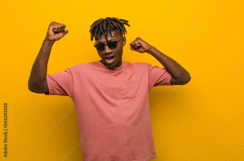 Fototapeta premium Young casual black man wearing sunglasses celebrating a special day, jumps and raising arms with energy.
