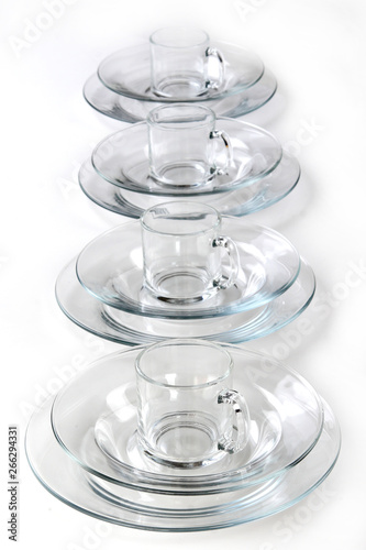 Crockery for four people of glass plates and cups on white background.