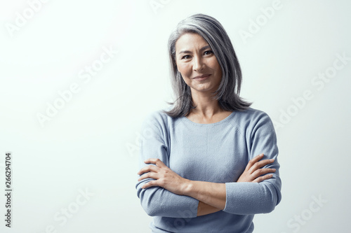 Beautiful woman with gray hair standing near the wall hands crossed