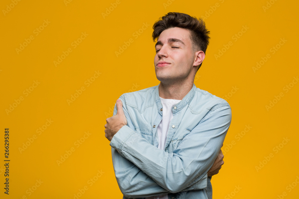 Fototapeta premium Young handsome student wearing a denim shirt hugs himself, smiling carefree and happy.