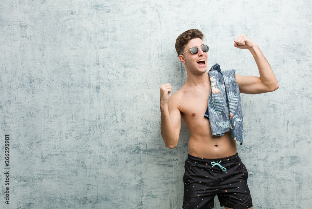 Young caucasian man wearing a swimsuit raising fist after a victory, winner concept.