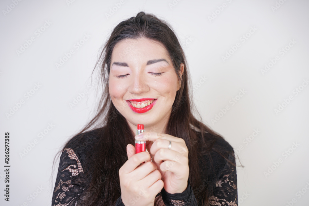 Asian happy woman paints her lips with lipstick on white studio background. Wrong try to do good self make up. Adult girl is learning to paint her face. Asian happy woman paints her lips with lipstick on white studio background. Wrong try to do good self make up. Adult girl is learning to paint her face.