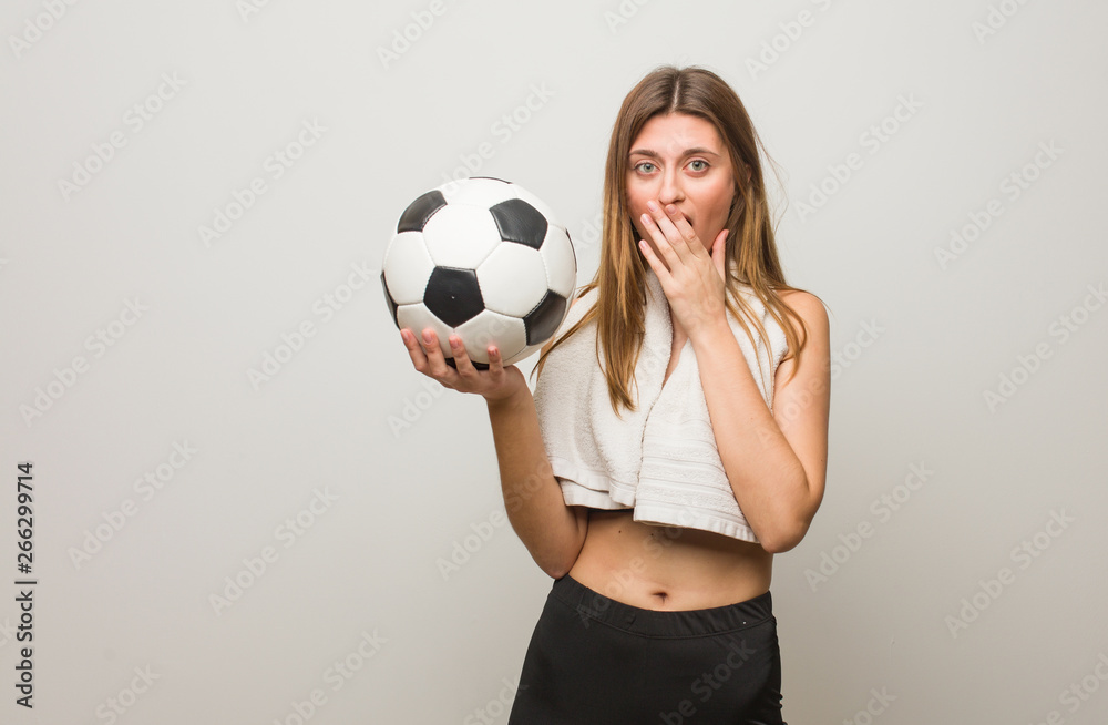 Young fitness russian woman very scared and afraid hidden. Holding a soccer ball.