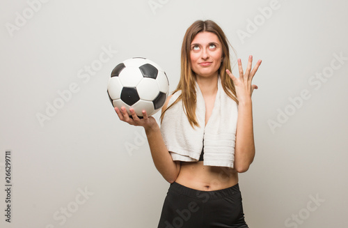 Young fitness russian woman very scared and afraid. Holding a soccer ball.