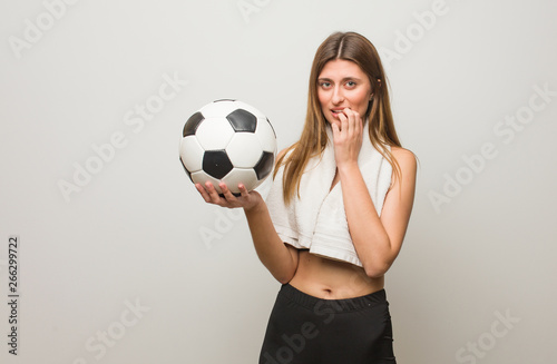 Young fitness russian woman biting nails, nervous and very anxious. Holding a soccer ball. © Asier