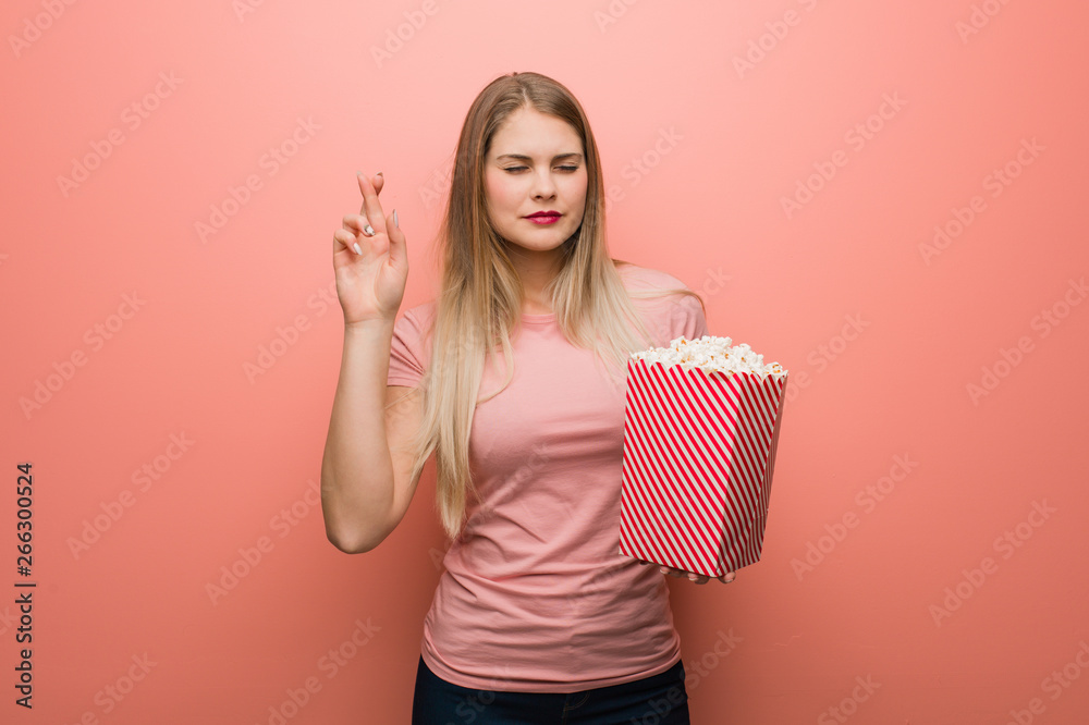 Young pretty russian girl crossing fingers for having luck. She is holding popcorns. Young pretty russian girl crossing fingers for having luck. She is holding popcorns.