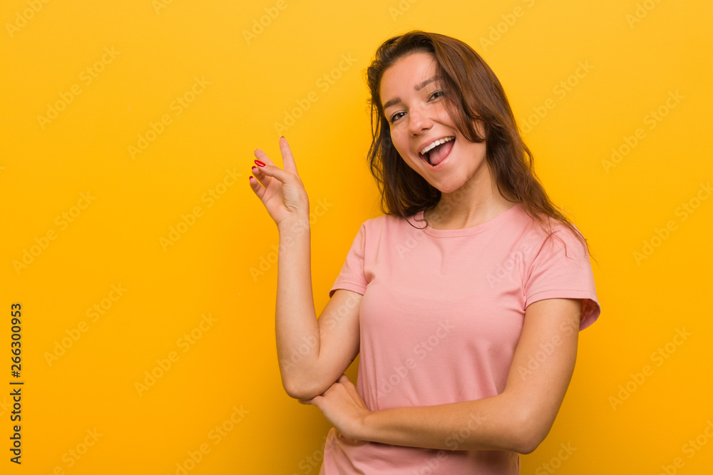 Young european woman isolated over yellow background joyful and carefree showing a peace symbol with fingers.
